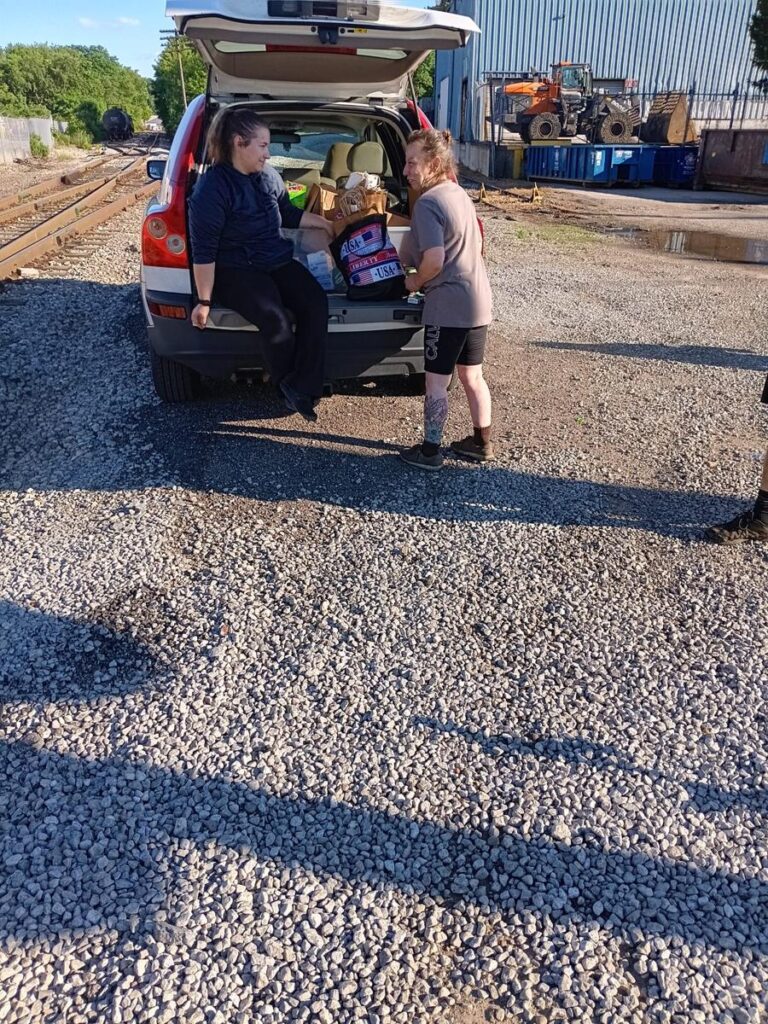 Supplies are handed out from an open car trunk during a Second Chance Village mobile outreach stop
