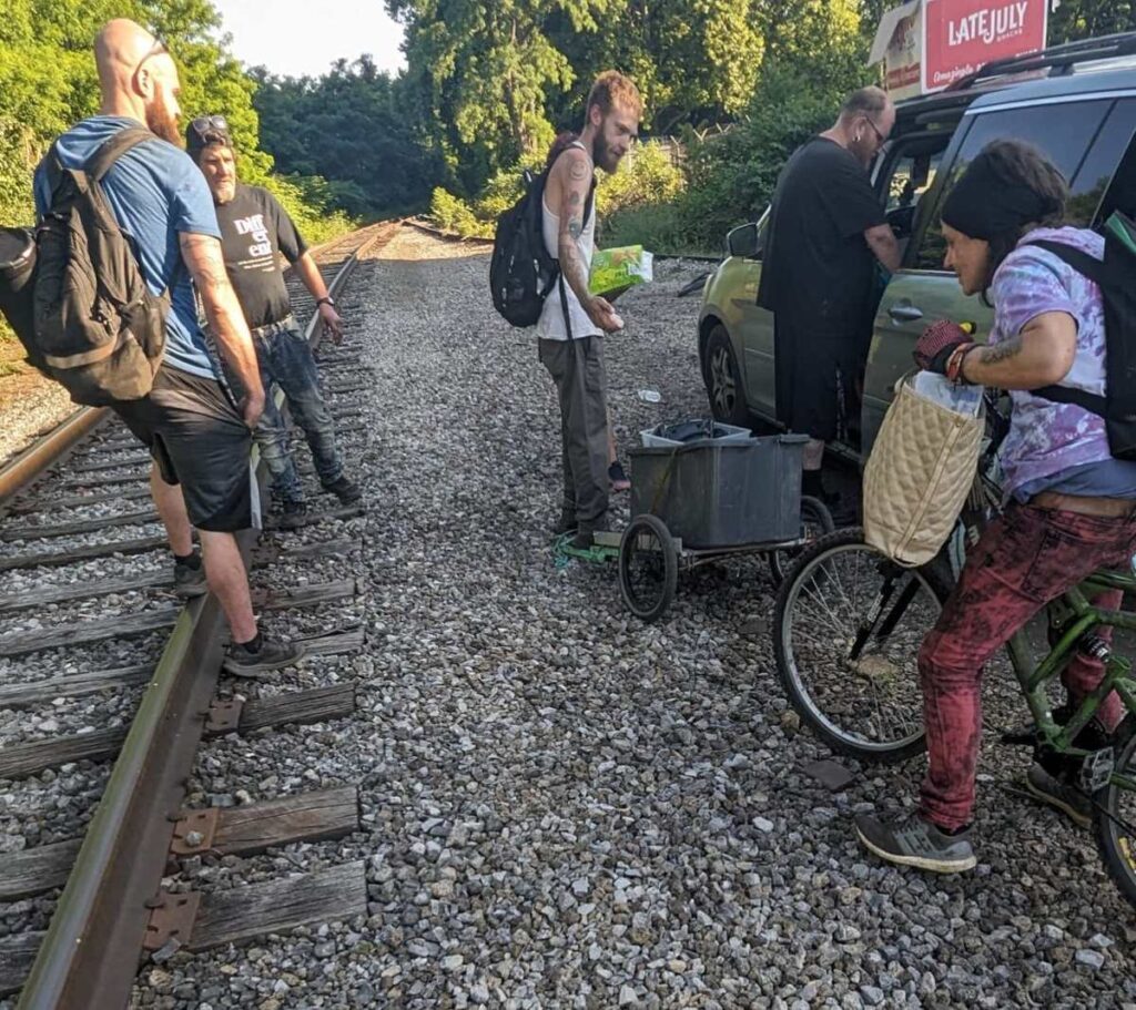 Second Chance Village volunteers bring supplies to people on bikes along a railroad track