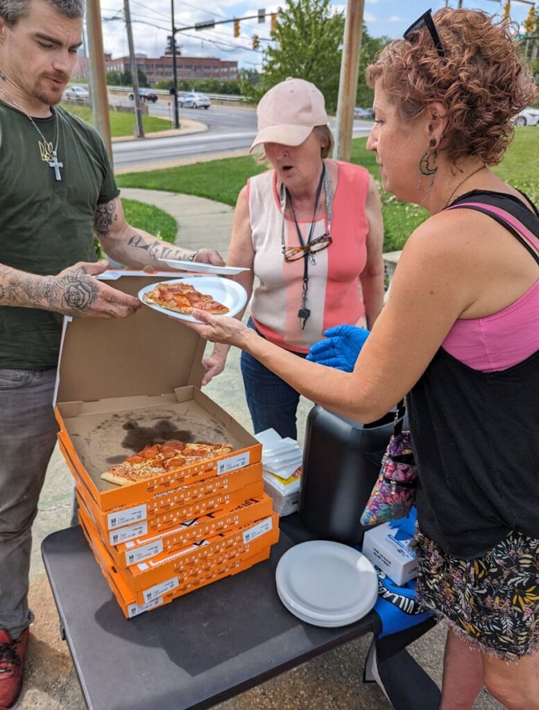 Second Chance Village volunteers serve pizza to community members at an outdoor table