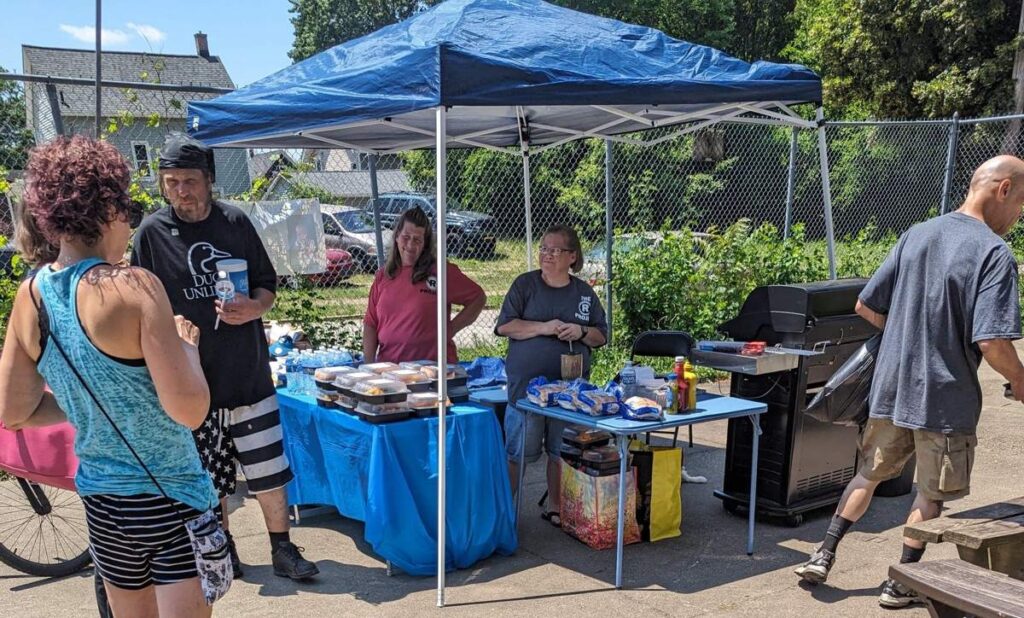 Second Chance Village volunteers run a pop-up supply table under a blue tent, with food and supplies laid out for anyone who stops by