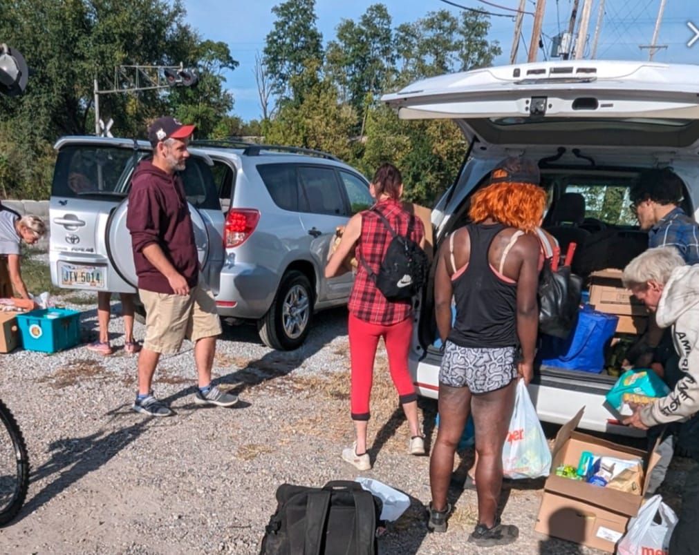 People gather at the open trunk of a Second Chance Village car during an outreach stop